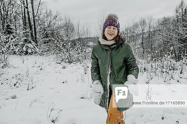 Laughing teenage girl holding snow while standing in snow during winter