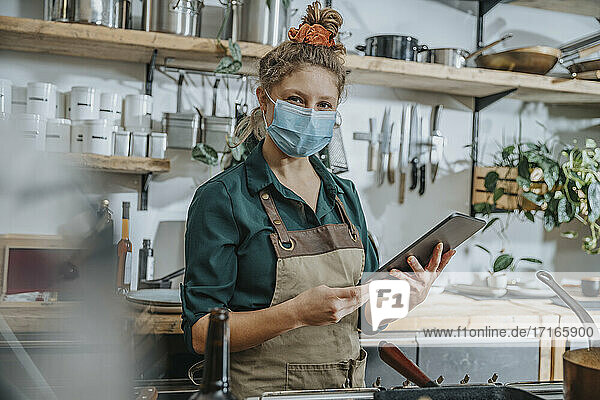 Female chef wearing protective face mask using digital tablet while standing in kitchen