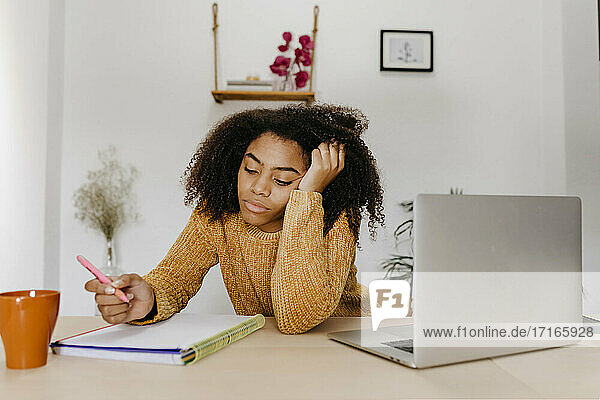 Junge Frau bei der Arbeit im Sitzen mit dem Kopf in den Händen im Heimbüro
