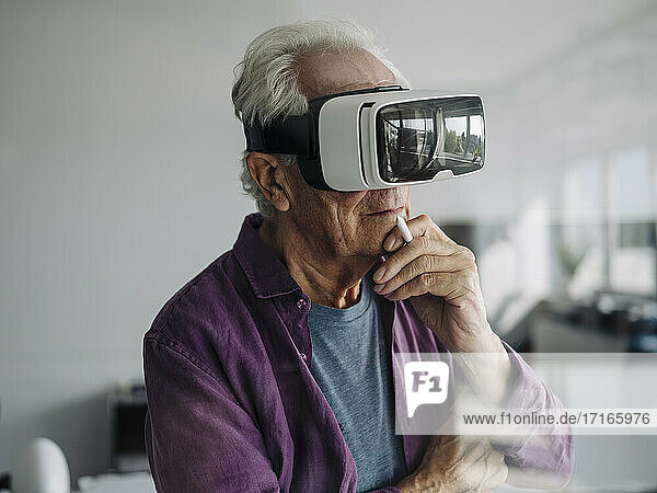 Nachdenklicher Geschäftsmann mit Hand auf Chi  der ein Virtual-Reality-Headset benutzt  während er im Büro steht