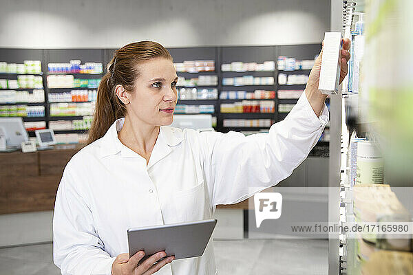 Female pharmacist with digital tablet checking medicine in store