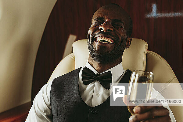 Junger männlicher Unternehmer lachend mit Champagner in der Hand in einem Privatjet