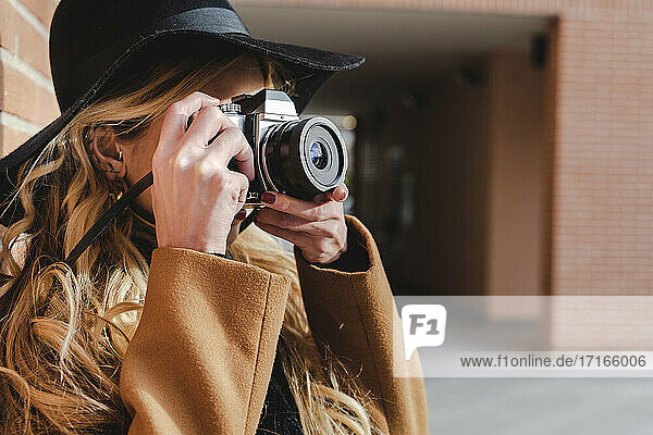 Young woman in hat filming through camera during sunny day