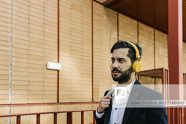 Businessman wearing headphones looking away while standing outdoors