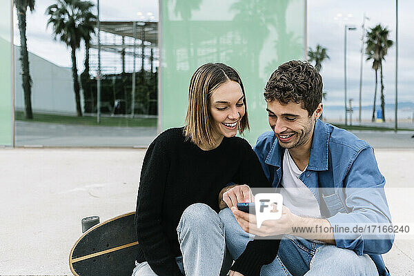 Lächelndes Paar  das im Freien auf sein Smartphone schaut