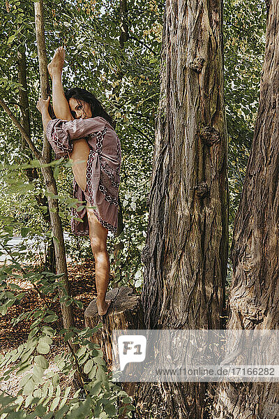 Woman stretching leg while doing yoga standing at forest