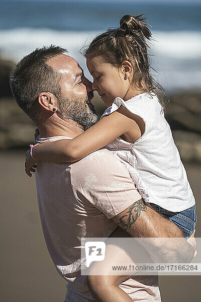 Smiling father carrying daughter at beach during sunny day
