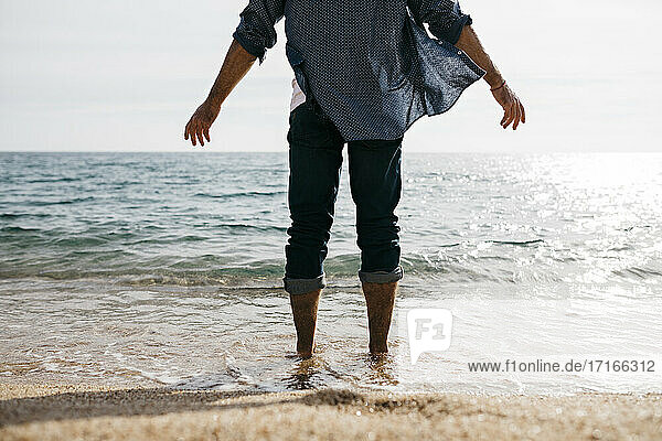 Älterer Mann steht am Rande des Wassers gegen den klaren Himmel am Strand