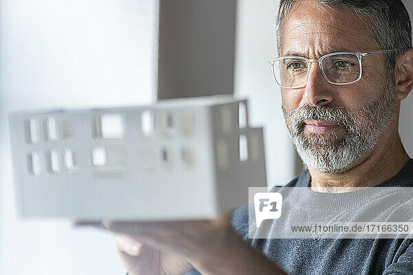 Geschäftsmann mit Brille  der ein architektonisches Modell untersucht  während er zu Hause steht