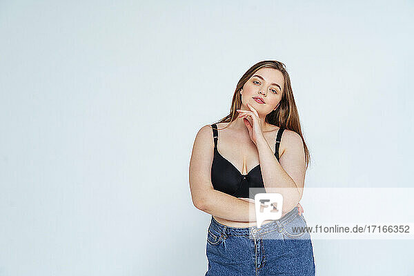 Confident curvy woman wearing bra and jeans standing against white background