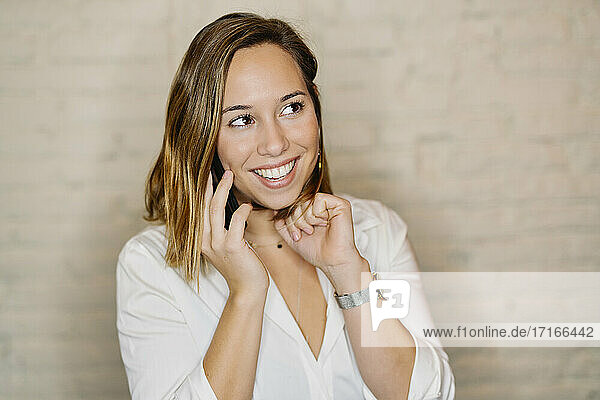 Smiling businesswoman talking over mobile phone against wall