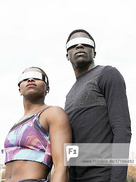 Sportler und Sportlerin mit Sonnenbrille schauen gegen den klaren Himmel weg