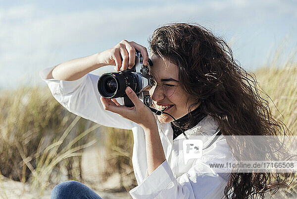 Young woman with long hair photographing through vintage camera at beach during sunny day