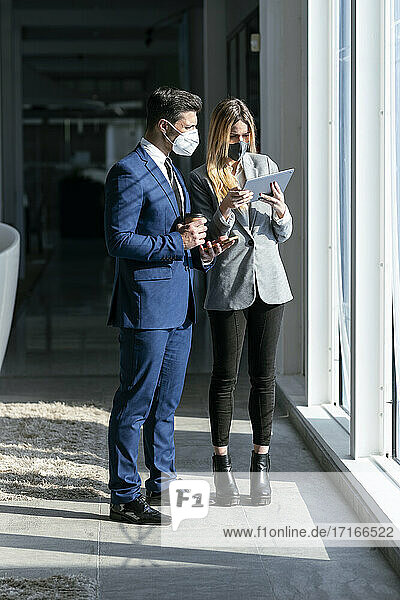 Berufstätige mit Gesichtsschutzmaske bei der Arbeit über einem digitalen Tablet im Stehen im Büro