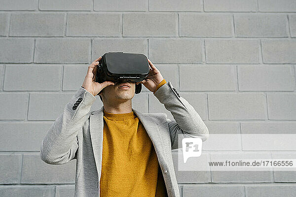 Mann benutzt ein Virtual-Reality-Headset  während er vor einer grauen Wand steht