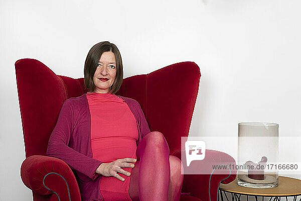 Woman with medium length hair sitting on armchair against white wall