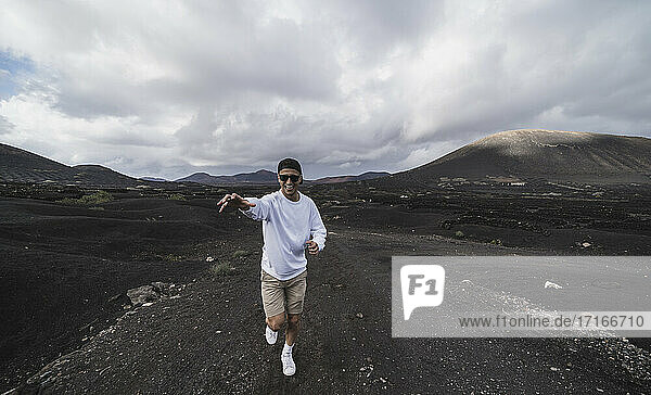 Smiling male tourist running while gesturing on black soil at El Cuervo Volcano  Lanzarote  Spain