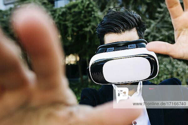 Businessman wearing virtual reality headset stretching hand while standing outdoors