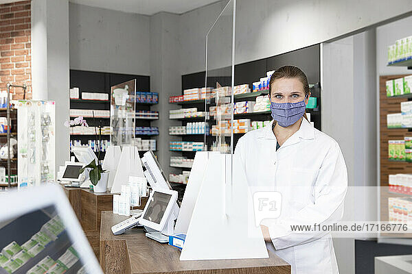 Female pharmacist in protective face mask standing at checkout in store