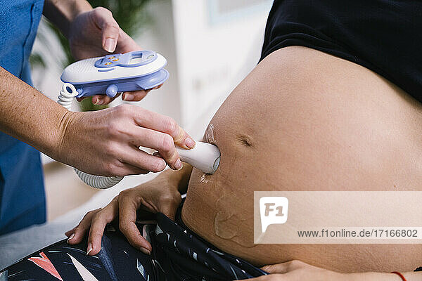 Midwife examining pregnant woman abdomen with ultrasound baby heartbeat monitor