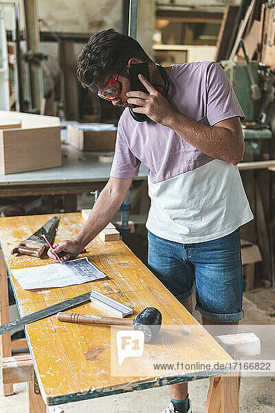 Male carpenter talking on smart phone while working in workshop