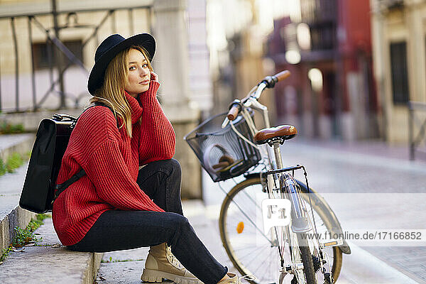 Thoughtful woman with hand on chin looking away while sitting on steps by bicycle