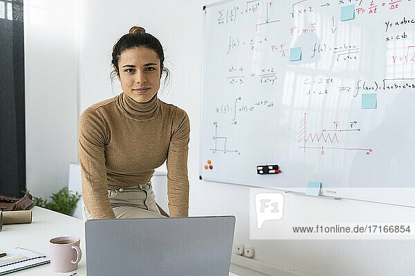 Studentin mit Laptop  die zu Hause am Whiteboard sitzt und lernt