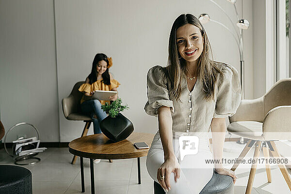 Smiling mother sitting on ottoman stool while daughter using digital tablet in background