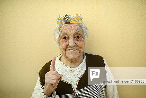 Nahaufnahme einer lächelnden älteren Frau mit Papierkrone  die gegen eine Wand gestikuliert