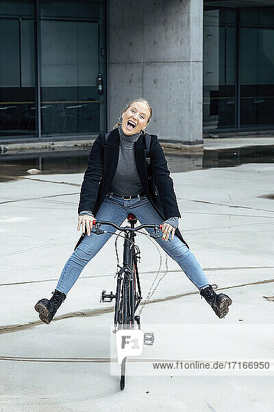 Cheerful woman doing cycling on road against structure