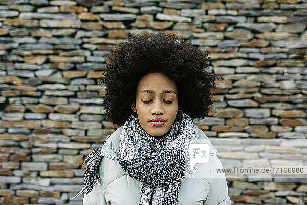 Afro junge Frau mit geschlossenen Augen gegen Steinwand im Winter