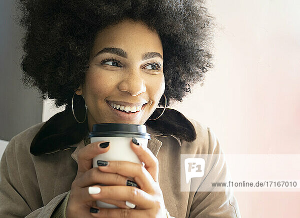 Smiling afro woman drinking coffee while sitting at cafe