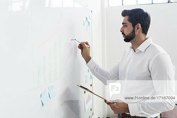 Männlicher Unternehmer  der ein Geschäftsdiagramm auf einem Whiteboard am Arbeitsplatz zeichnet