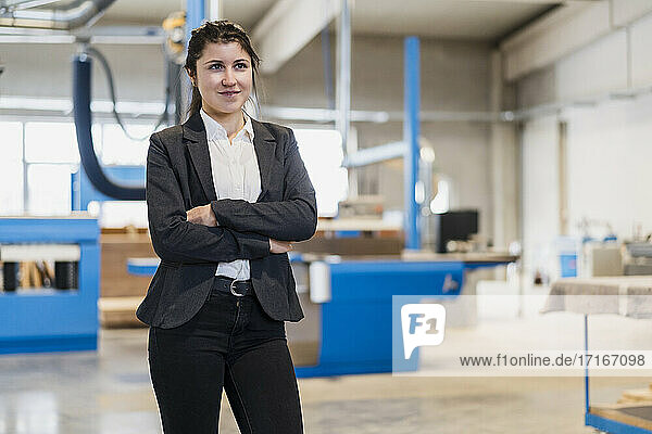 Confident young businesswoman with arms crossed looking away while standing at industry