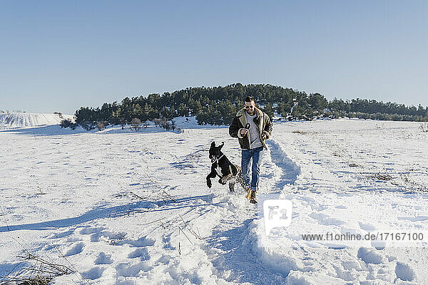Playful man with dog running in snow on sunny day