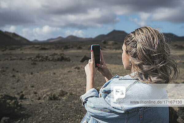 Junge Frau  die ein Foto mit ihrem Handy macht  während sie am Vulkan El Cuervo steht  Lanzarote  Spanien