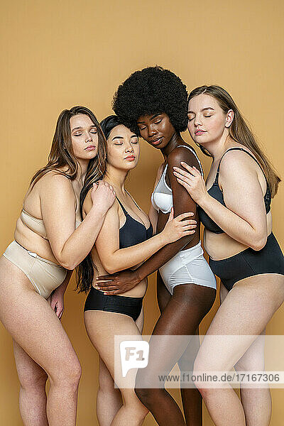 Gruppe von weiblichen Modellen mit geschlossenen Augen in Dessous  die sich gegenseitig umarmen  vor gelbem Hintergrund
