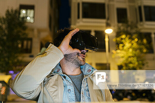 Mann lächelt  während er im Freien sitzend ein Virtual-Reality-Headset benutzt