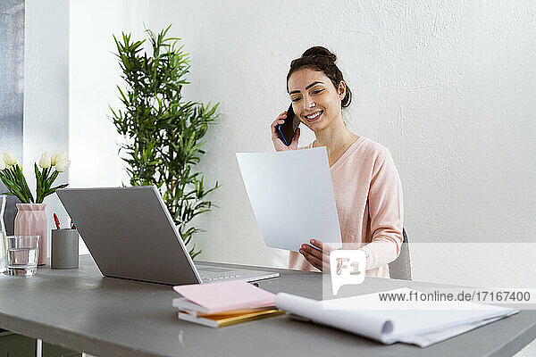 Smiling woman talking on mobile phone while sitting by table at home office