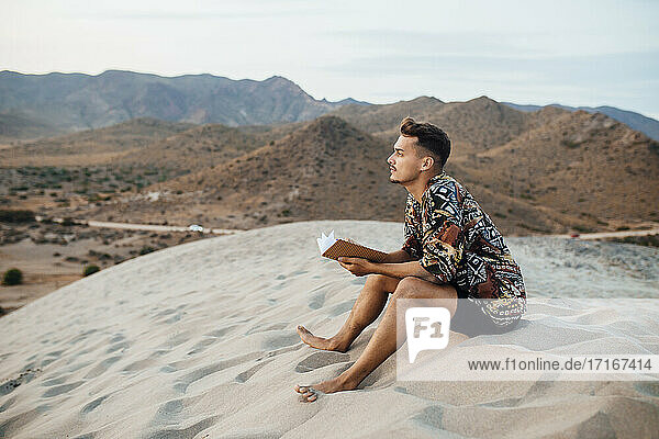 Junger Mann  der in der Wüste von Almeria  Tabernas  Spanien  über ein Buch nachdenkt