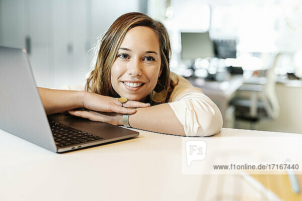 Nahaufnahme einer lächelnden Geschäftsfrau  die sich an einen Laptop auf dem Schreibtisch lehnt und nachdenkt