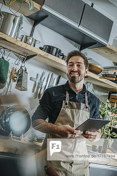 Smiling male chef using digital tablet while standing in kitchen
