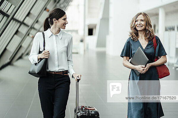 Smiling female professionals discussing while walking in corridor at office