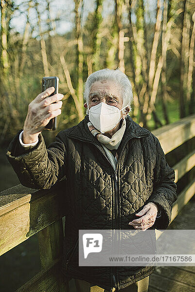 Ältere Frau  die ein Selfie mit ihrem Mobiltelefon macht  während sie auf einer Fußgängerbrücke während der COVID-19 steht