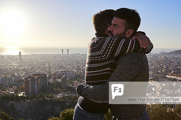 Gay boyfriends embracing while standing against cityscape during sunrise  Bunkers del Carmel  Barcelona  Spain
