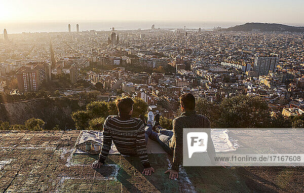 Gay boyfriends looking at crowded cityscape while sitting on viewpoint  Bunkers del Carmel  Barcelona  Spain