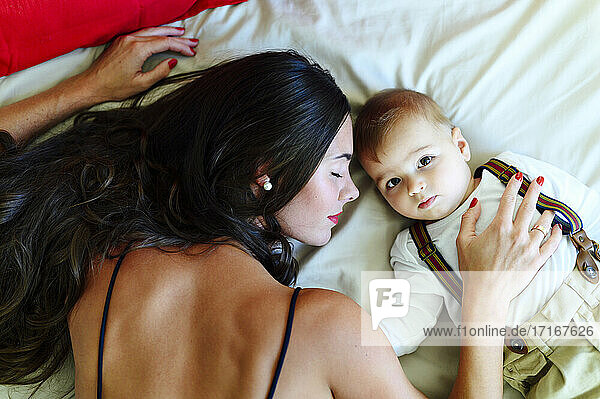 Young woman resting with baby boy while lying on bed