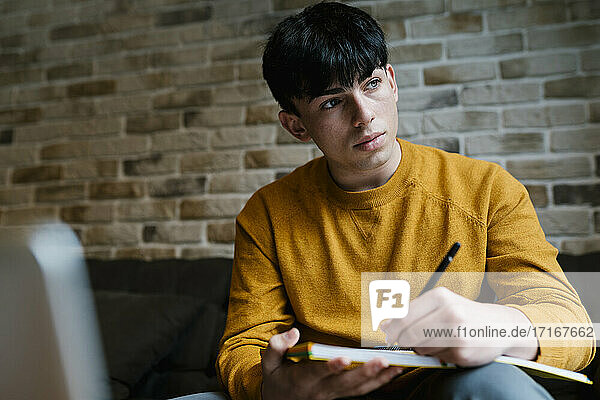 Young thoughtful man with book looking away while sitting on sofa at cafe
