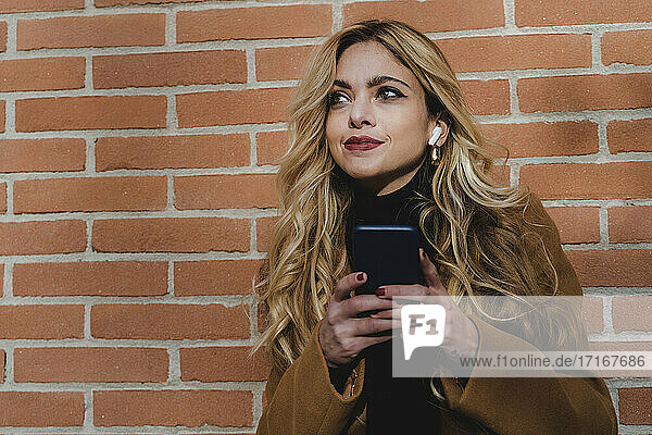 Blond woman with smart phone listening music while looking away