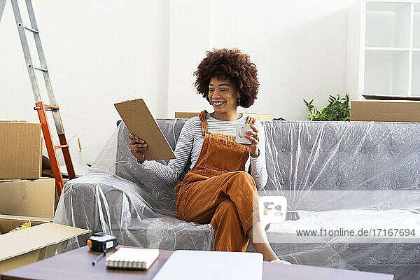Lächelnde Frau mit Checkliste auf einem Klemmbrett in ihrer neuen Wohnung